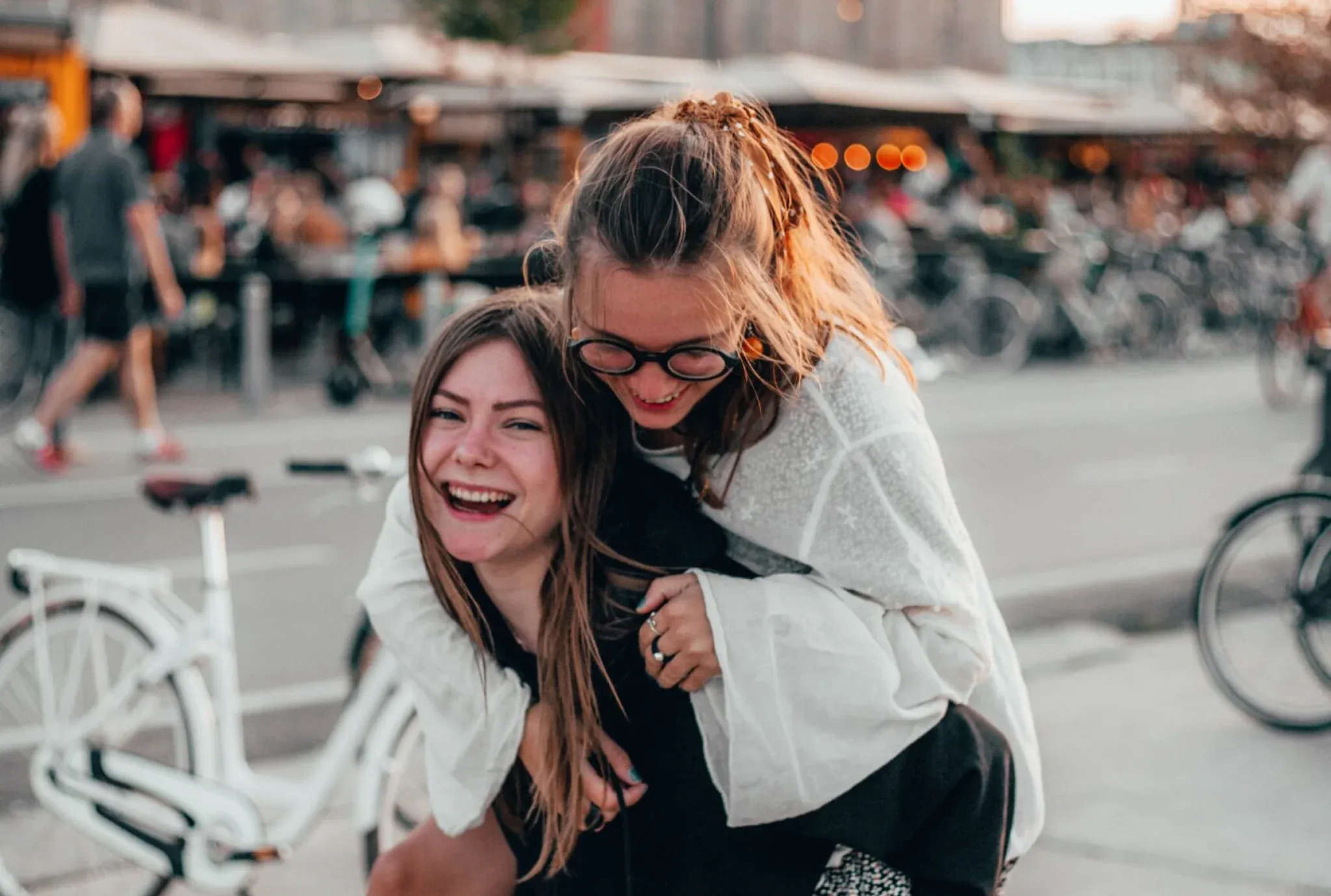Dos universitarias caminando por el centro de la ciudad, sonriendo, una llevando a la otra a caballito.
