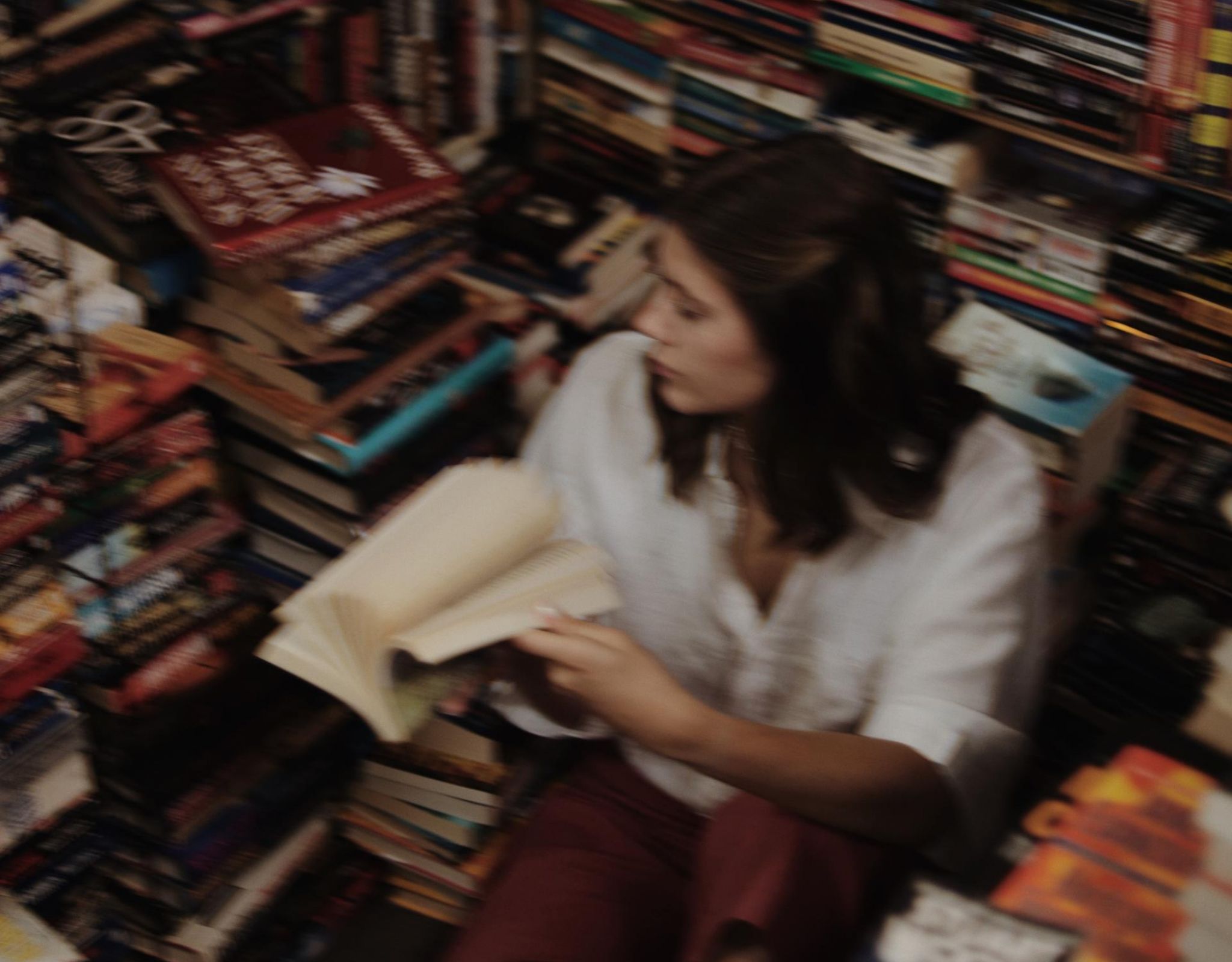 Young woman sitting on the floor in library amongst a pile of books