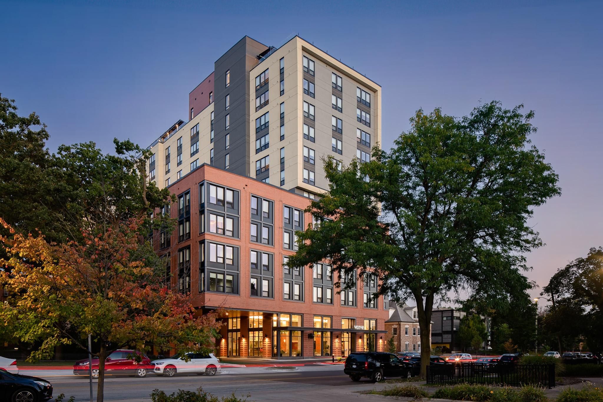 Verve Ann Arbor modern multi-story apartment building with large windows, trees, and cars parked along the street at dusk.