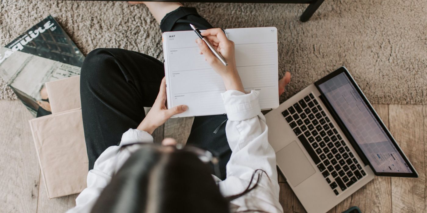 Person sitting and writing into a notebook, applying study tips. They are surrounded by a laptop and books.