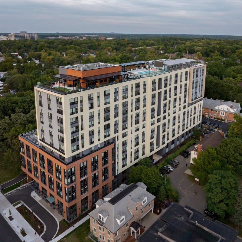 Verve Ann Arbor, moderno edificio de apartamentos de mediana altura rodeado de árboles y viviendas residenciales, visto desde arriba.