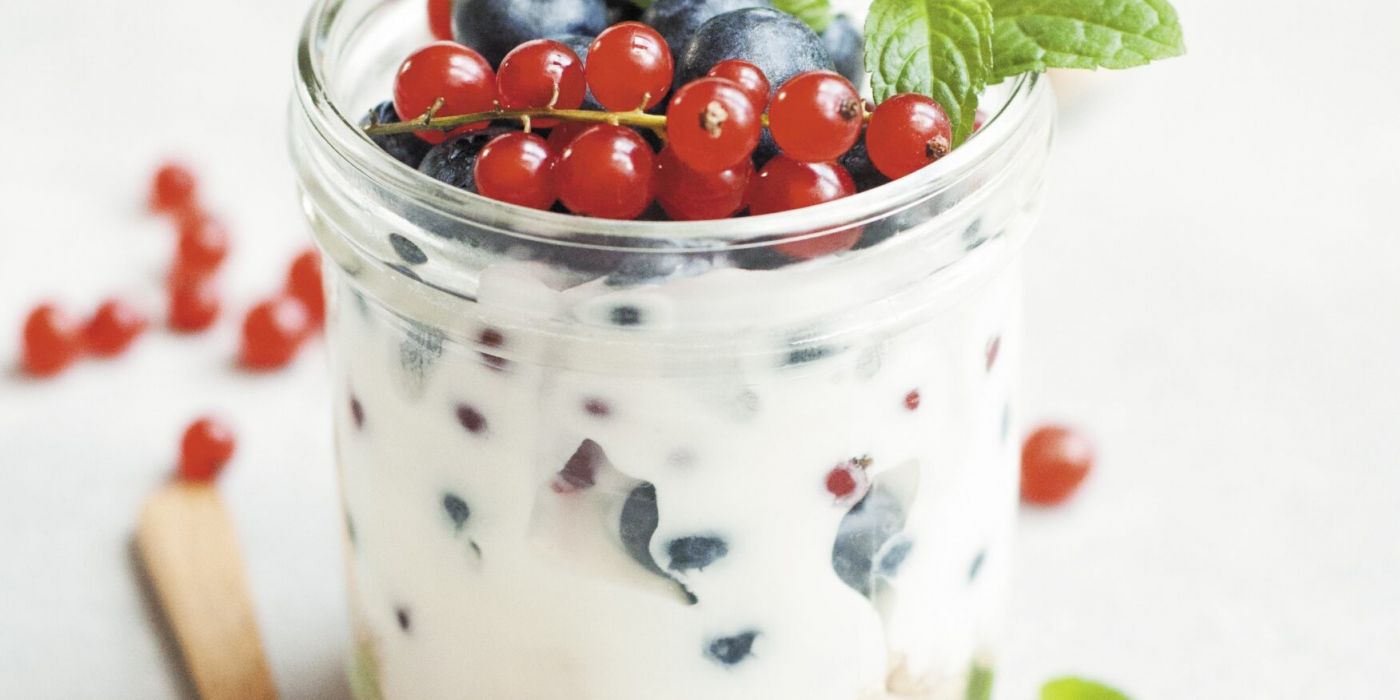 Glass jar full of yogurt and topped with various berries